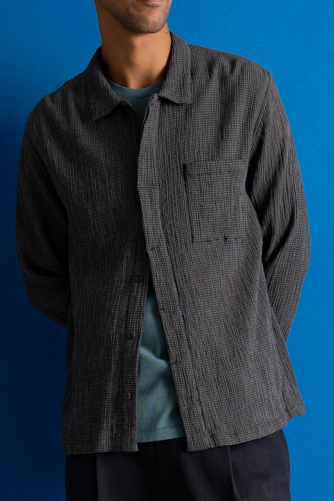 Man wearing textured grey checkered shirt and a dark green cap against a bright blue background