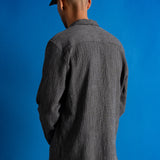 Man wearing textured grey checkered shirt and a dark green cap against a bright blue background