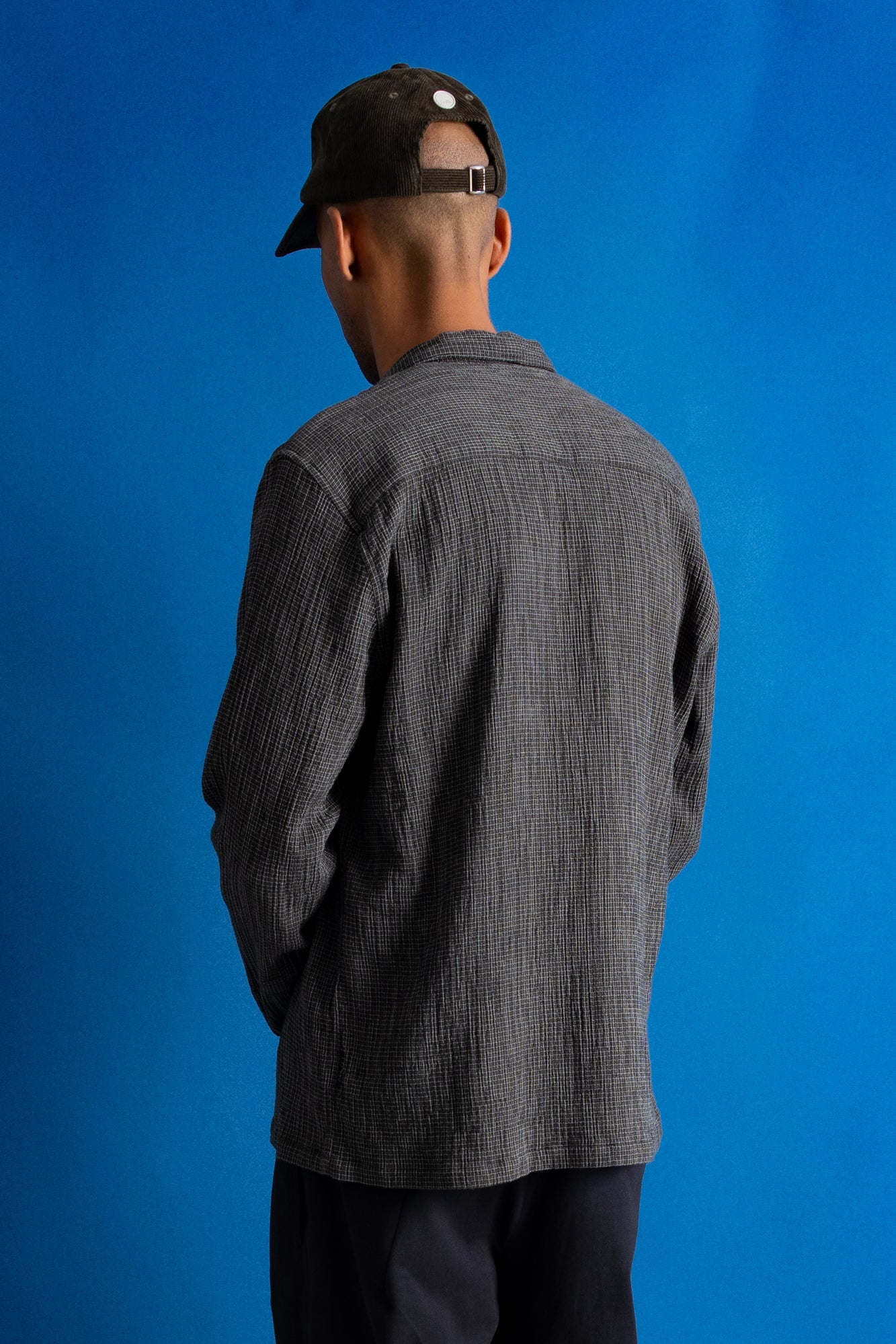 Man wearing textured grey checkered shirt and a dark green cap against a bright blue background