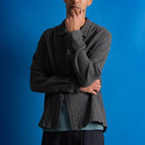 Man wearing textured grey checkered shirt and a dark green cap against a bright blue background