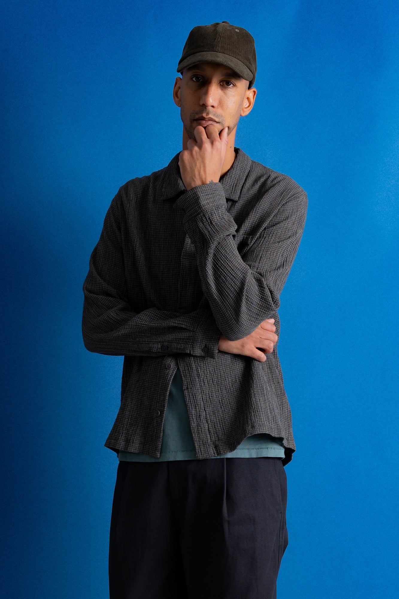 Man wearing textured grey checkered shirt and a dark green cap against a bright blue background