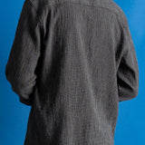 Man wearing textured grey checkered shirt and a dark green cap against a bright blue background