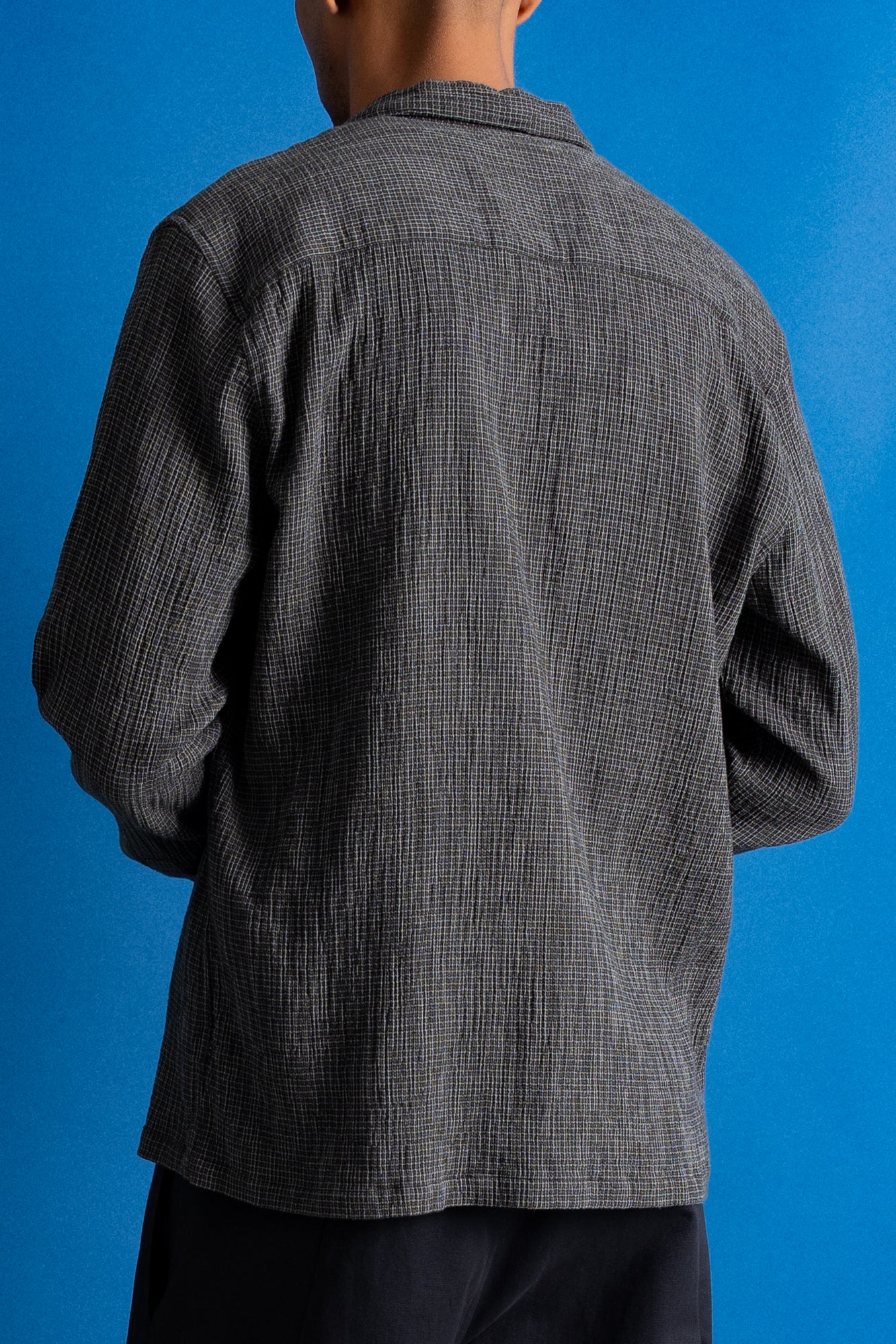 Man wearing textured grey checkered shirt and a dark green cap against a bright blue background