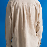 A person viewed from the back wearing a light beige linen button-up shirt and dark trousers, set against a solid blue background.