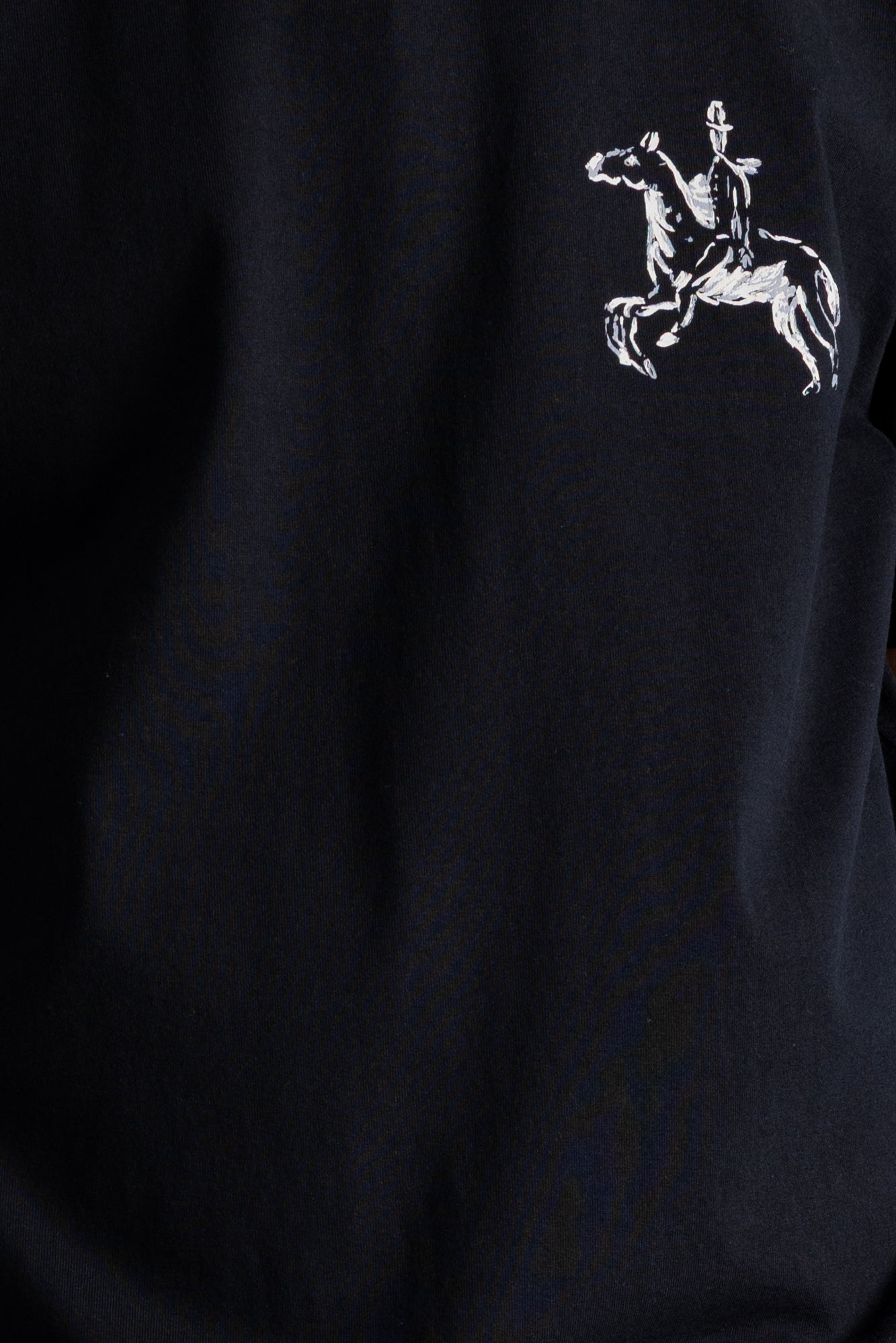 Close-up of a dark navy blue fabric with a small white embroidered graphic of a rider on a horse on the chest.