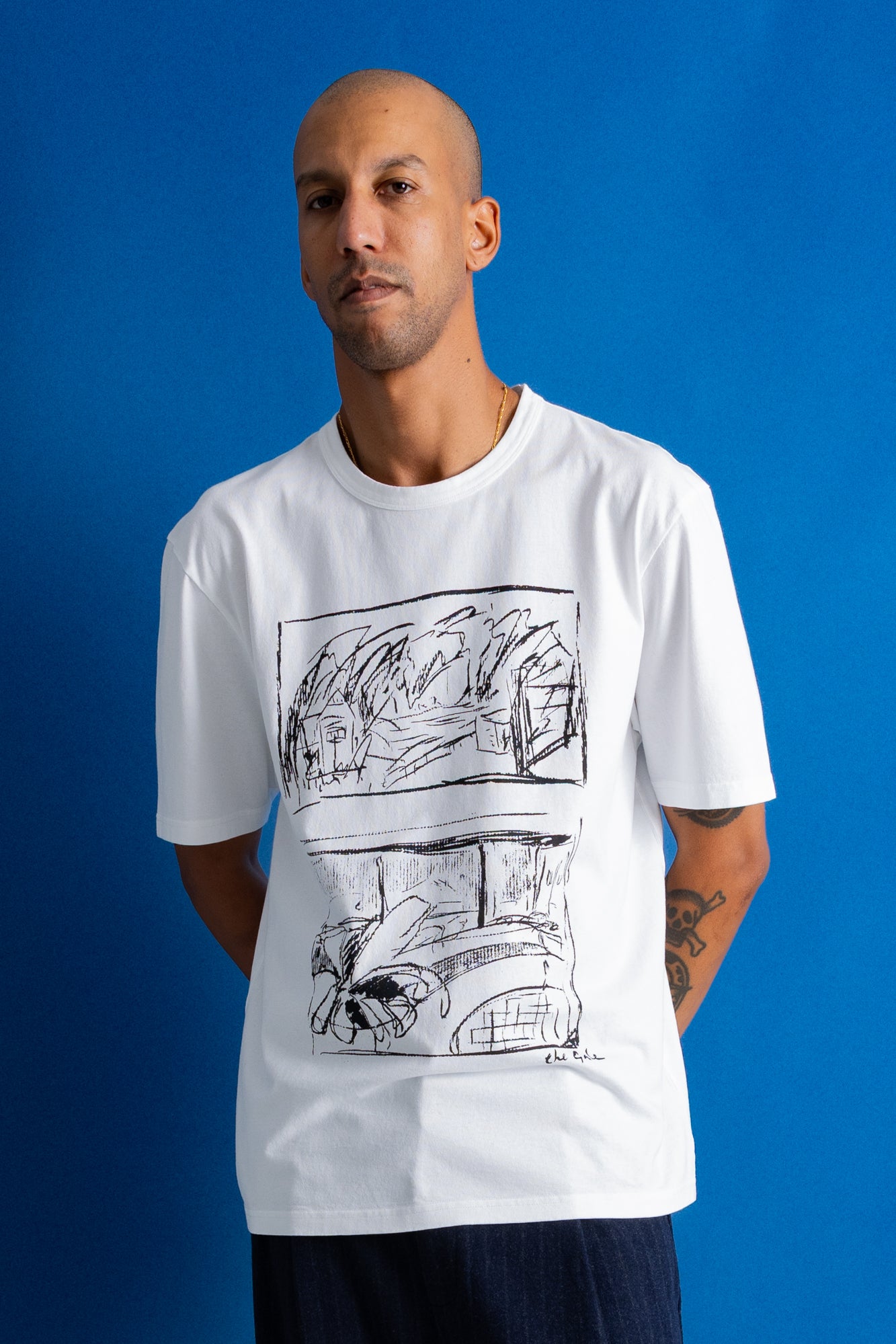 A man wearing a white crewneck t-shirt with a black line art graphic print, posed against a solid blue background.