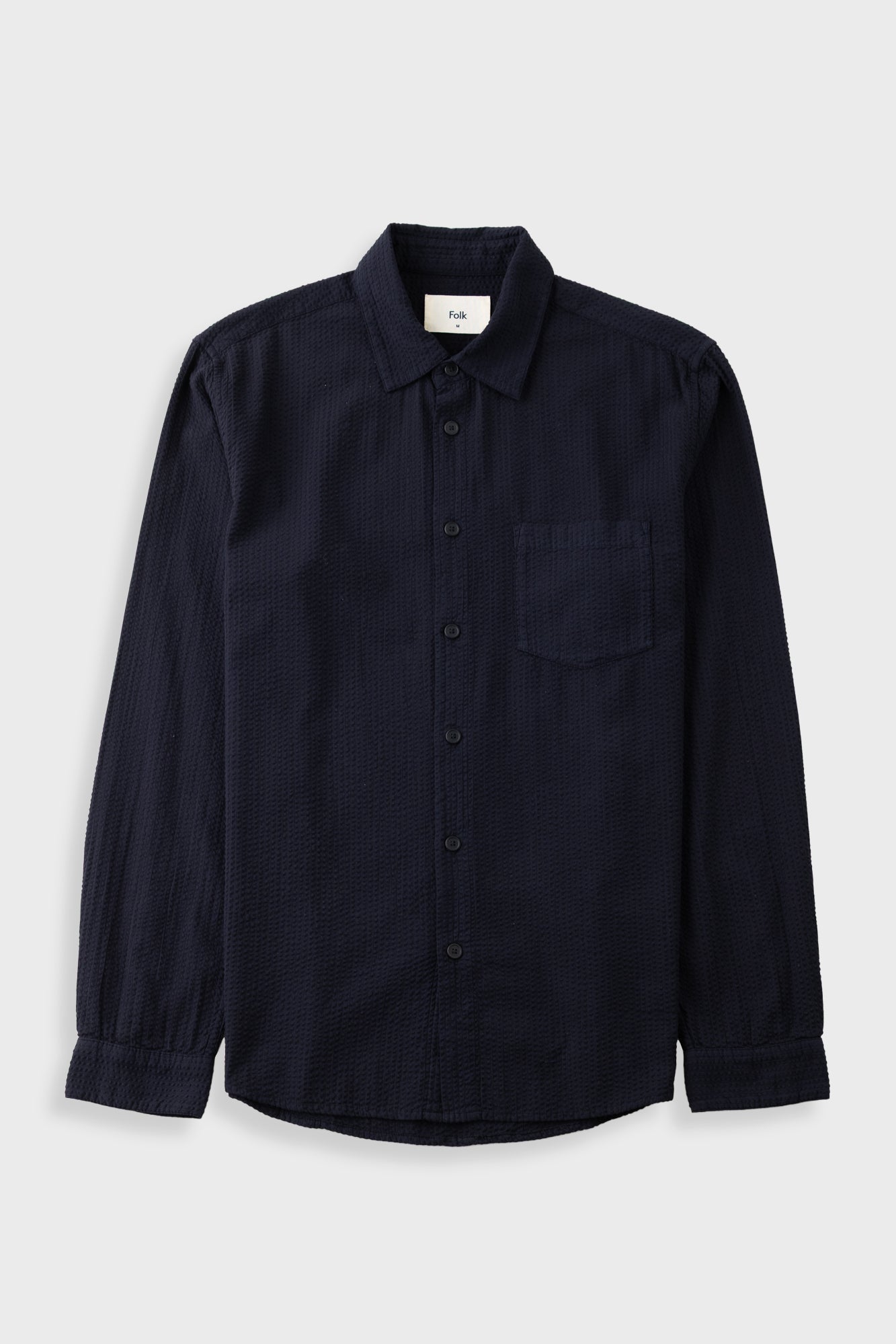 A dark navy blue long-sleeve button-up shirt with a single chest pocket, laid flat against a light gray background.