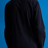 A person shown from the back wearing a dark navy textured long-sleeve button-up shirt and dark pants against a solid blue background.