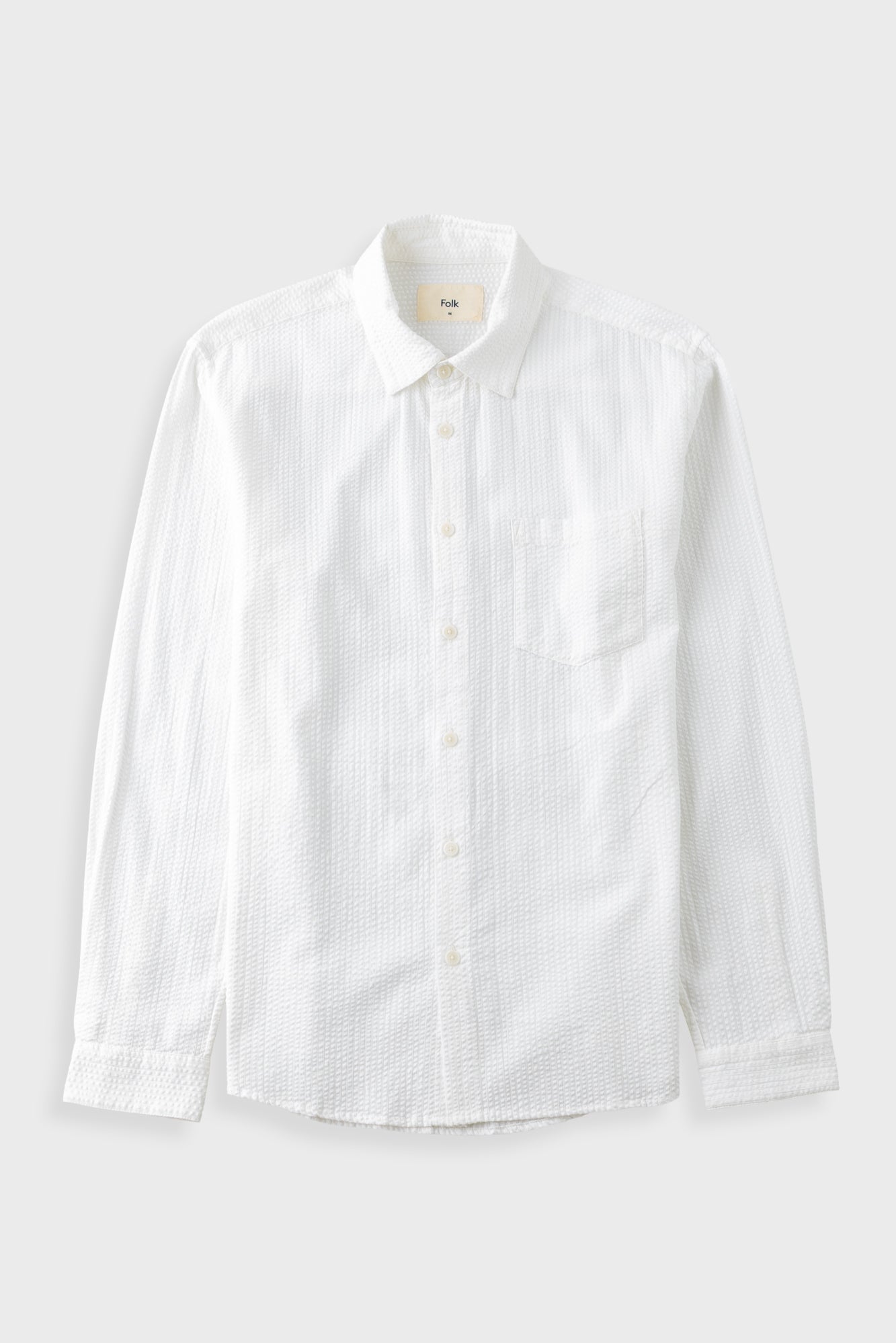 A white long-sleeve button-down shirt with a subtle textured pattern, featuring a single chest pocket and a classic collar, shown against a light gray background.