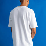 A man viewed from behind wearing a plain white short-sleeve crewneck t-shirt and blue jeans, standing against a solid blue studio background.