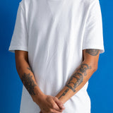 A person wearing a plain white short-sleeve crew-neck t-shirt, standing against a solid blue background.