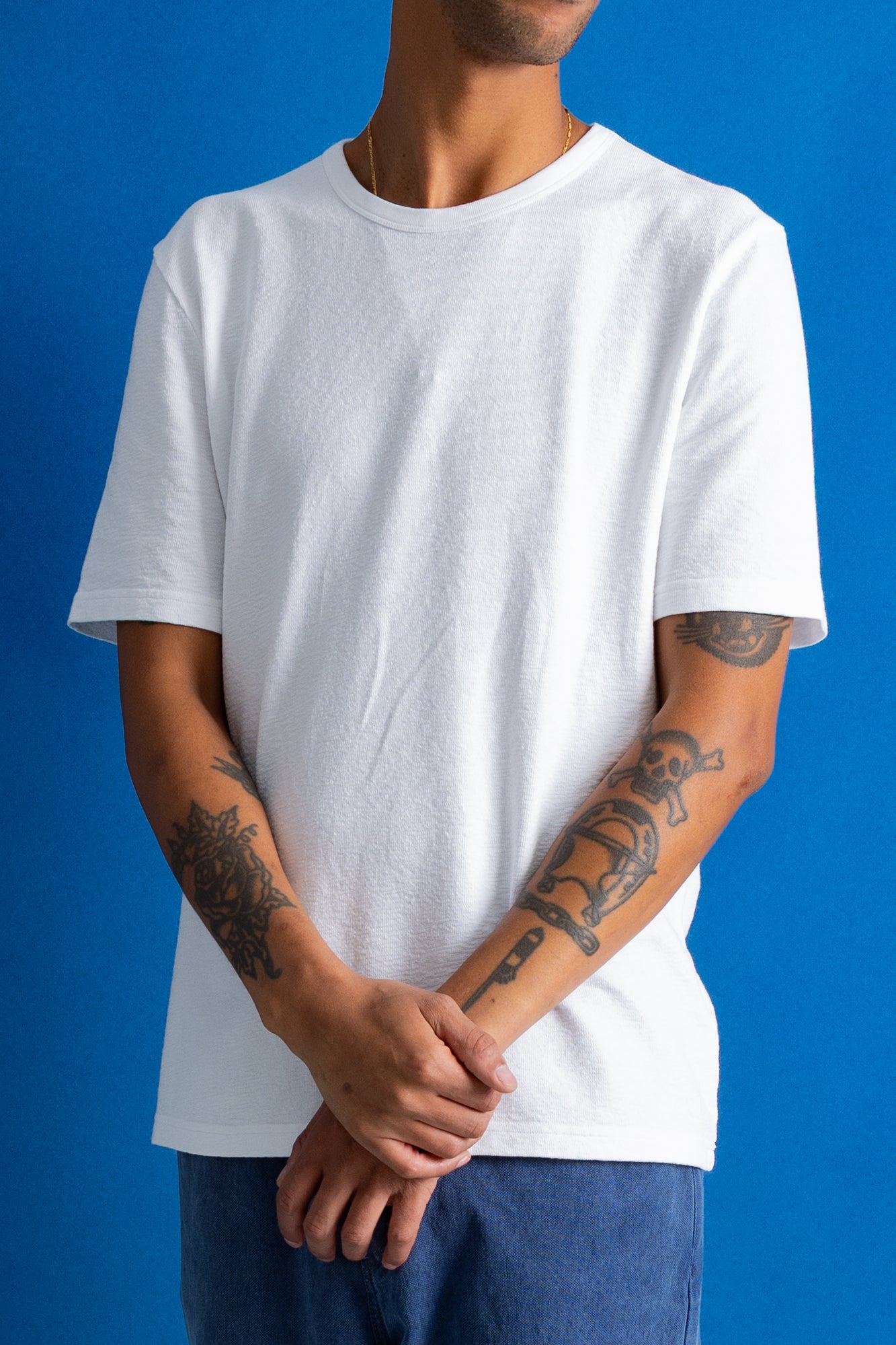 A person wearing a plain white short-sleeve crew-neck t-shirt, standing against a solid blue background.
