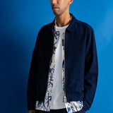 A man wearing a dark navy blue jacket over a white t-shirt with a blue and white graphic print, standing against a solid blue background.