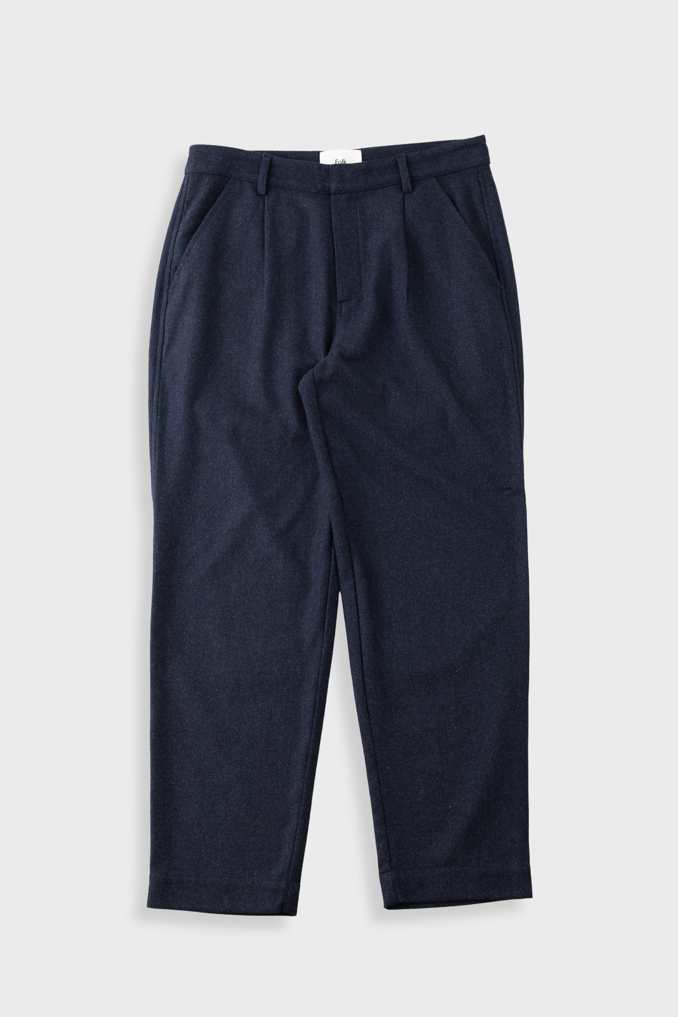A pair of dark navy blue trousers with a textured fabric, featuring a flat front and side pockets, laid flat against a light gray background.