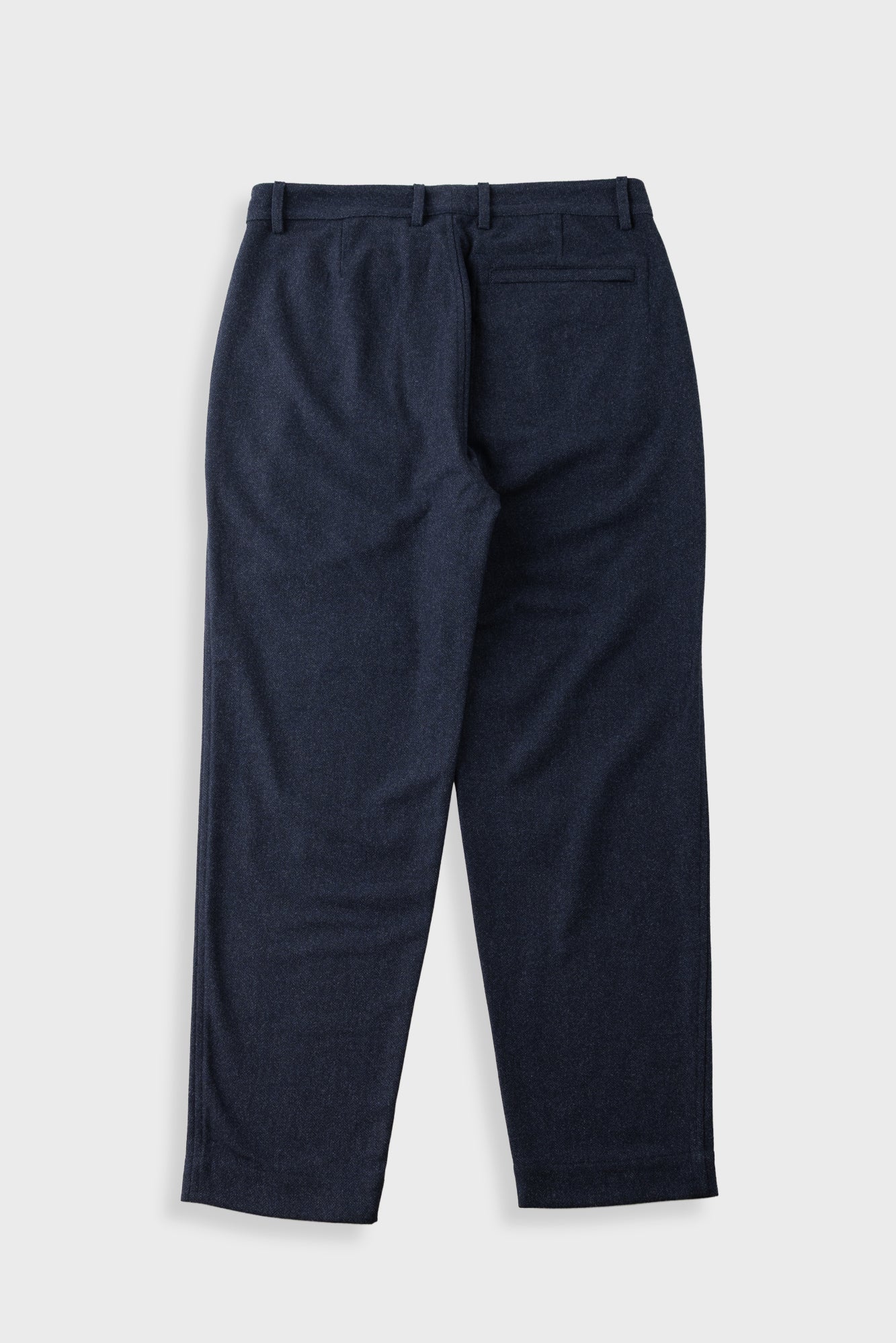 A pair of dark navy blue trousers shown from the back, featuring a button closure and belt loops, laid flat against a light gray background.