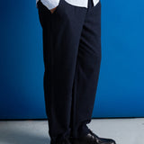 A person wearing dark navy trousers, a white dress shirt, and black leather shoes, standing against a solid blue backdrop.