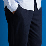 A close-up of a person wearing dark navy trousers and a light blue shirt against a solid blue background.