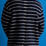 A person shown from the back wearing a navy blue knit sweater with horizontal off-white stripes, set against a solid blue background.
