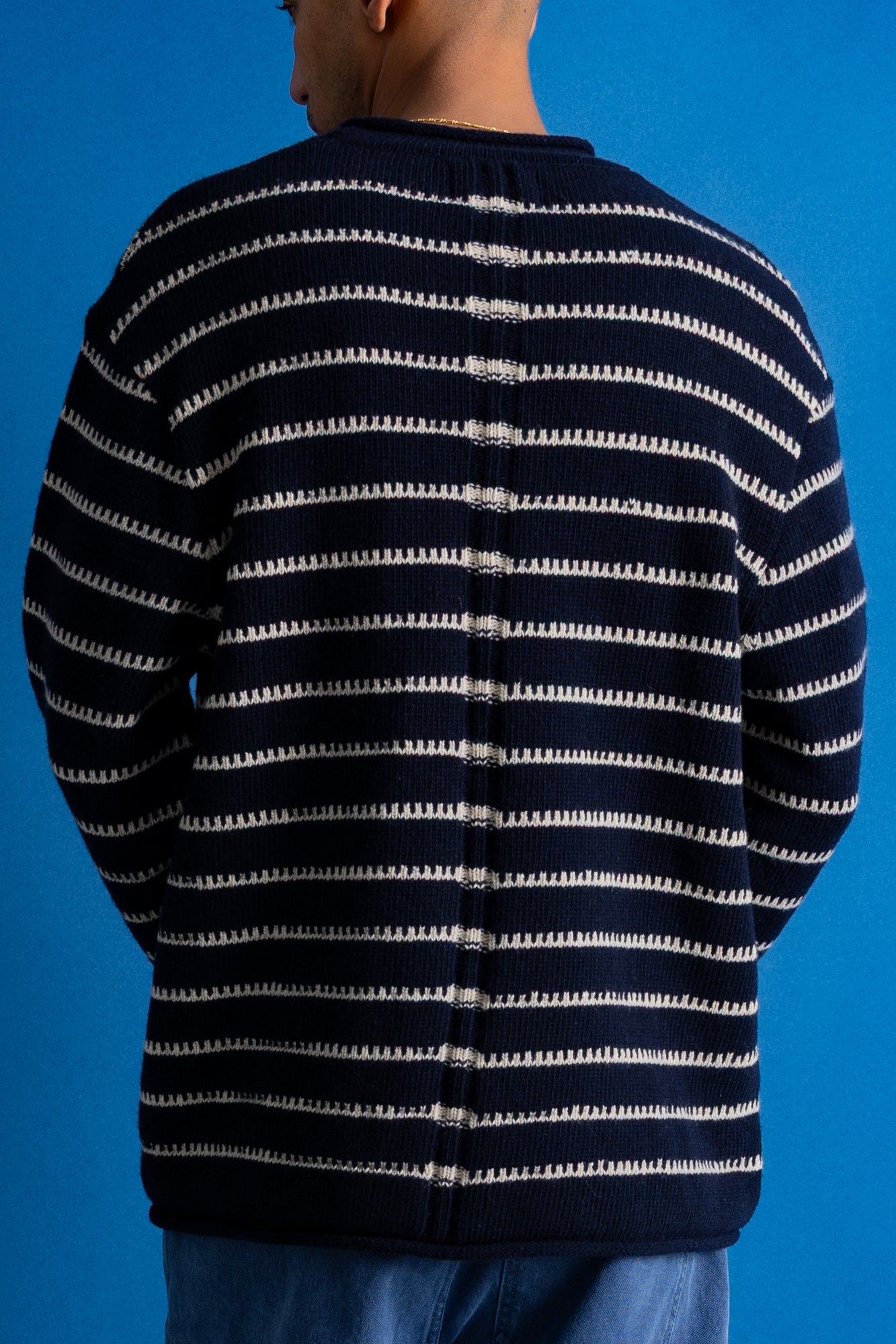 A person shown from the back wearing a navy blue knit sweater with horizontal off-white stripes, set against a solid blue background.