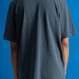 A person shown from the back wearing an oversized slate blue-gray t-shirt and brown pants, set against a solid blue background.