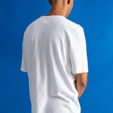 A man viewed from behind wearing a plain white short-sleeve t-shirt and dark pants, standing against a solid blue background.