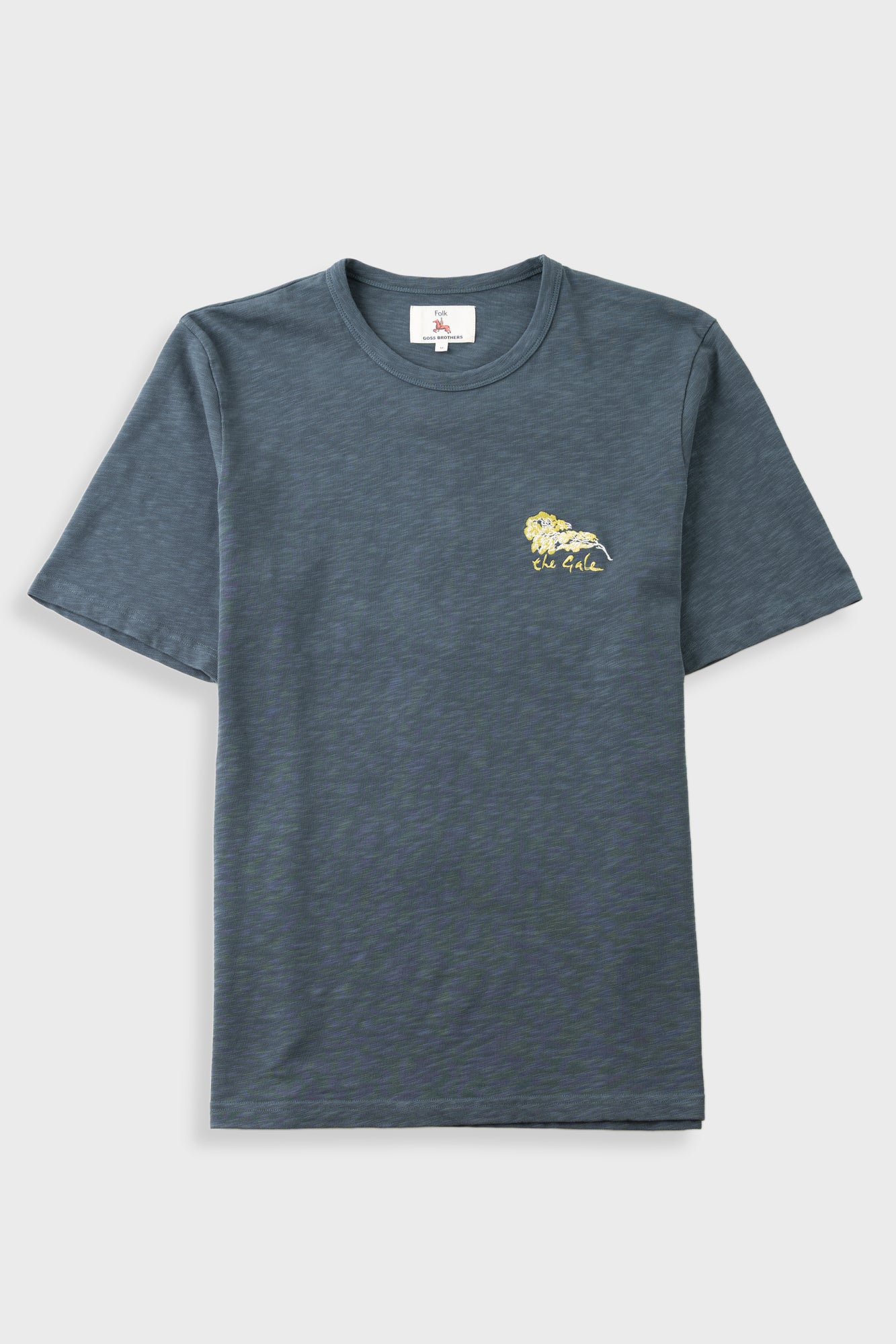A dark heather gray crewneck t-shirt with a small yellow embroidered lion logo and 'The Gold' text on the left chest, displayed against a light gray background.
