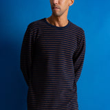 A man wearing a dark navy long-sleeve shirt with thin orange horizontal stripes, standing against a solid blue background.