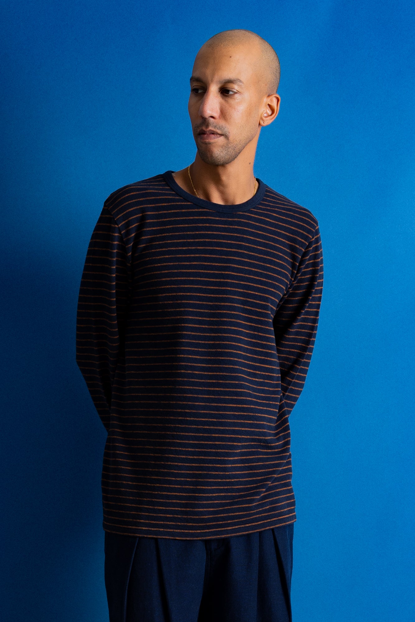 A man wearing a dark navy long-sleeve shirt with thin orange horizontal stripes, standing against a solid blue background.