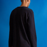 A man viewed from behind wearing a dark navy long-sleeve shirt with thin orange horizontal stripes, set against a solid blue background.