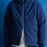 A man wearing a navy blue hooded zip-up jacket, shown from the chin down against a solid blue background.