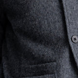 Close-up of a dark gray textured wool-blend jacket with a buttoned front and a pocket, showing the fabric texture and button details.