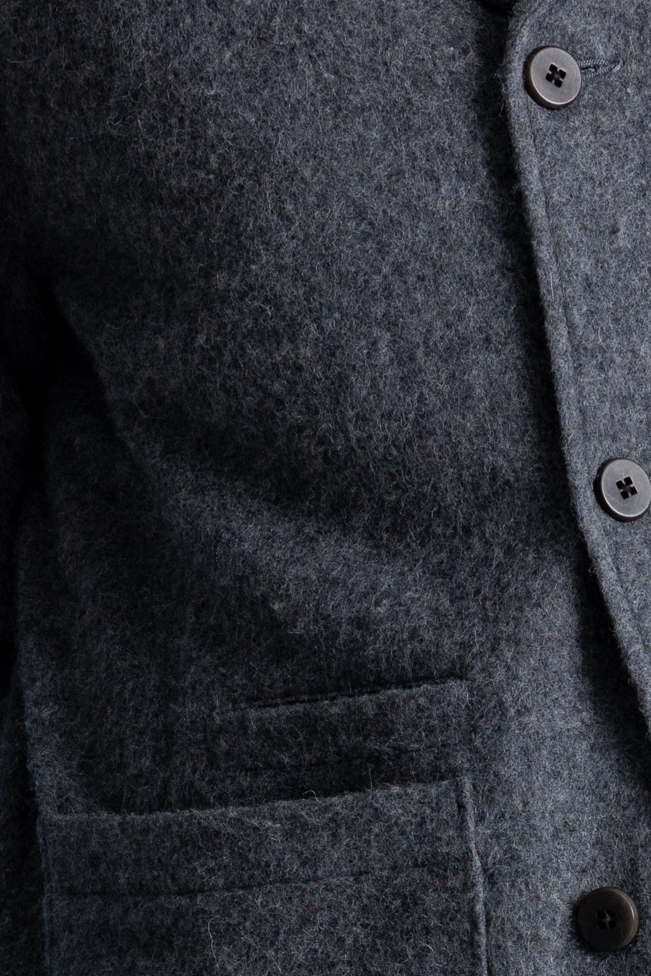 Close-up of a dark gray textured wool-blend jacket with a buttoned front and a pocket, showing the fabric texture and button details.