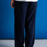 A person shown from the back wearing dark navy wide-leg denim pants, a white t-shirt, and black boots, standing against a vibrant blue studio background.