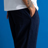 A close-up side view of a person wearing dark navy pinstriped trousers and a white t-shirt, standing against a solid blue background.