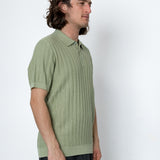 Man wearing a green ribbed knit polo shirt against a white background