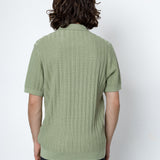 Person wearing a green ribbed sweater against a white background
