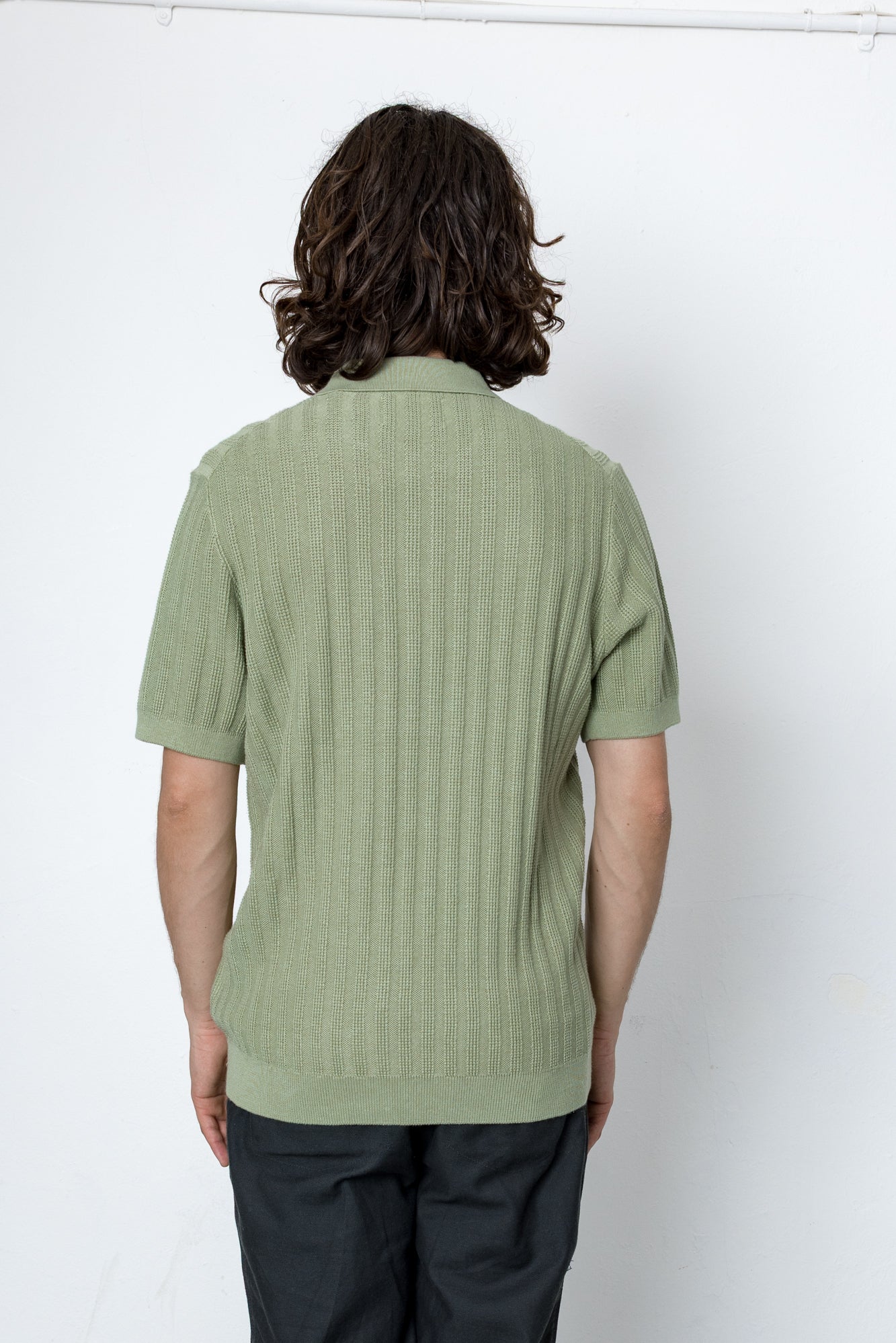 Person wearing a green ribbed sweater against a white background