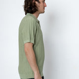 Man wearing a green shirt and black pants against a white background