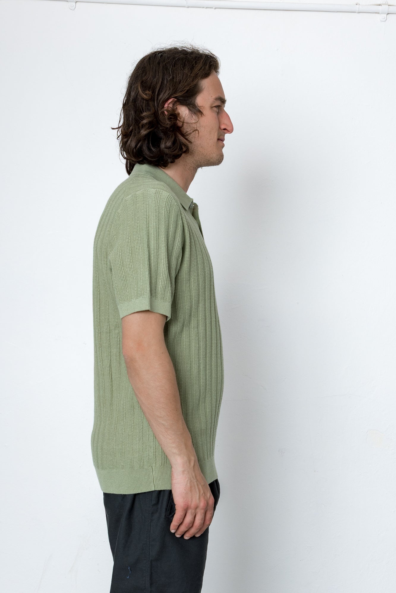 Man wearing a green shirt and black pants against a white background